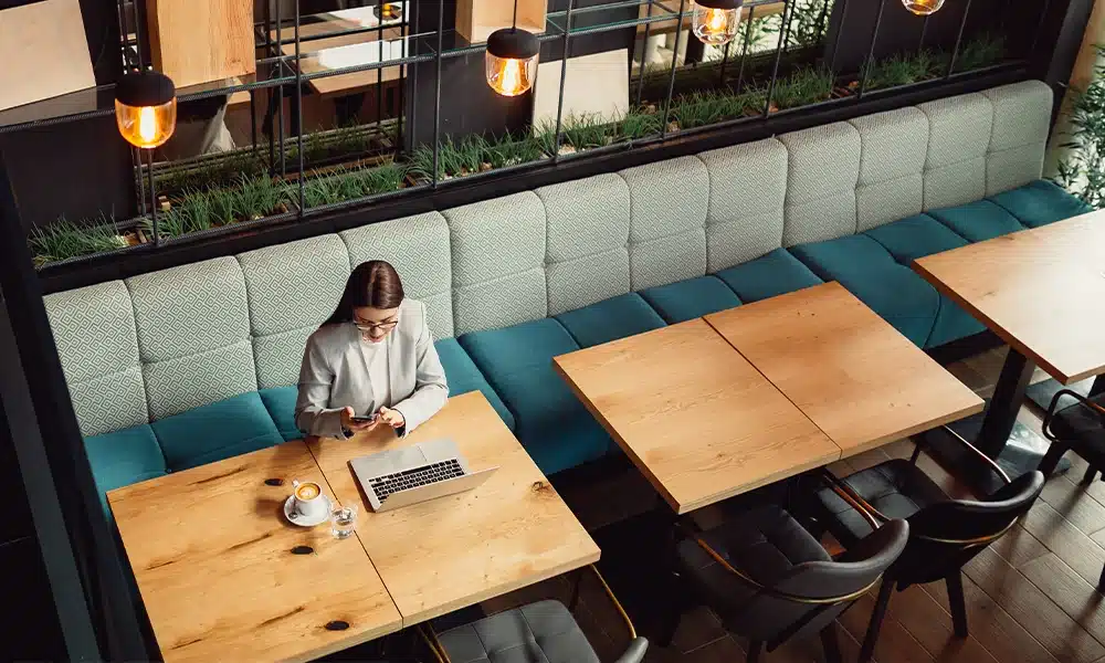 anquette seating along a glass wall with café tables opposite and a woman sitting with a coffee