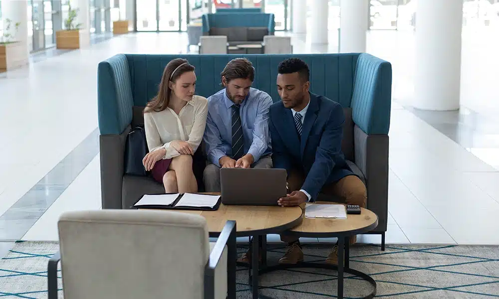 three business people sit on a high back enclosed booth seat in a large open plan office lobby