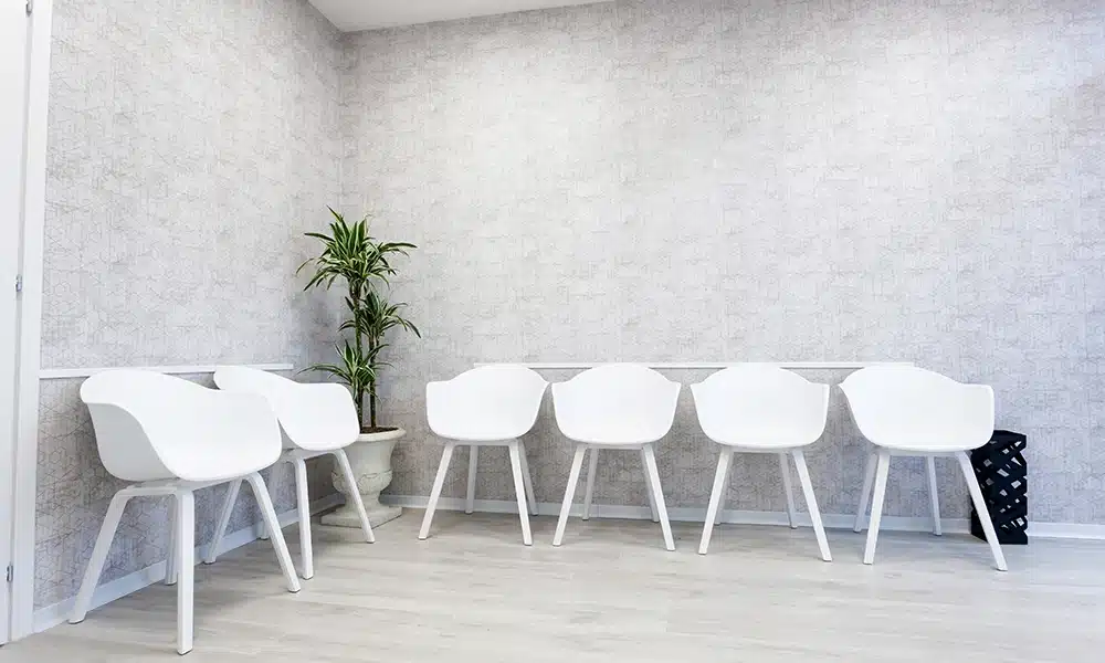 very bright white dental clinic waiting room, white plastic chairs are lined up against the wall