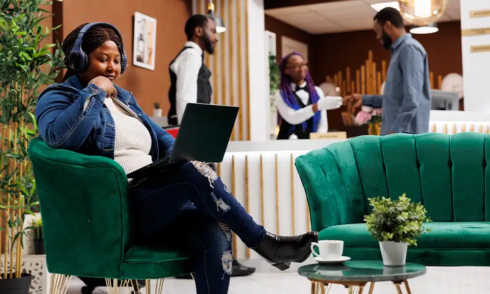 a lady sits on a velvet green booth chair in a busy hotel lobby