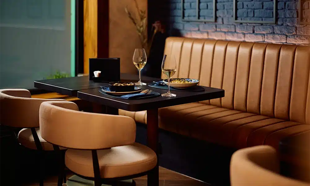 Fluted back booth seating with rustic upholstered chairs in a dark luxury restaurant setting