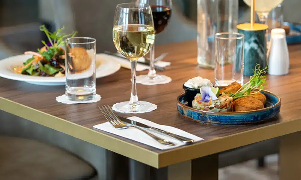 Light oak wood table top with a gold edging, tablewear and food on top of the table set for a restaurant