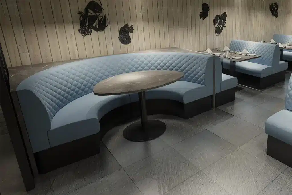 Dimly lit bar interior with half-round quilted booth seating and a distressed marble-effect table.