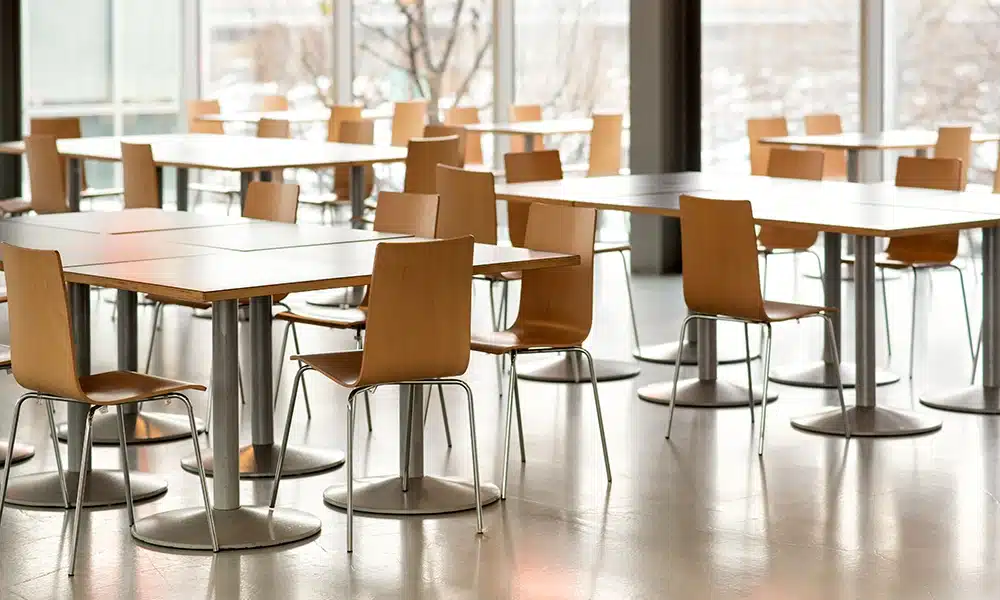 a large school cafeteria with matching metal and wood chairs around large tables for dining