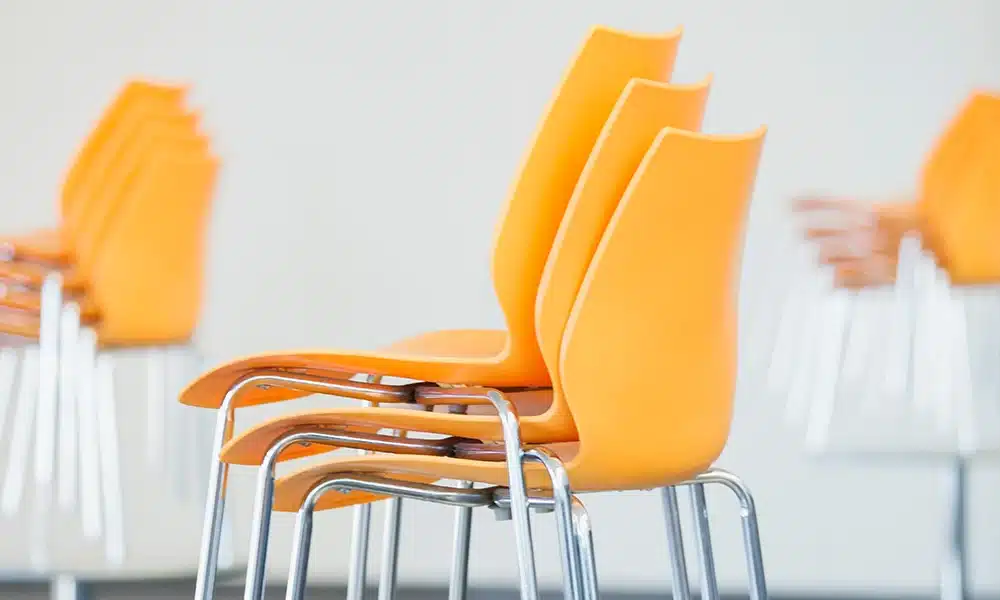 three orange plastic and metal framed chairs stacked on top of eachother on a table