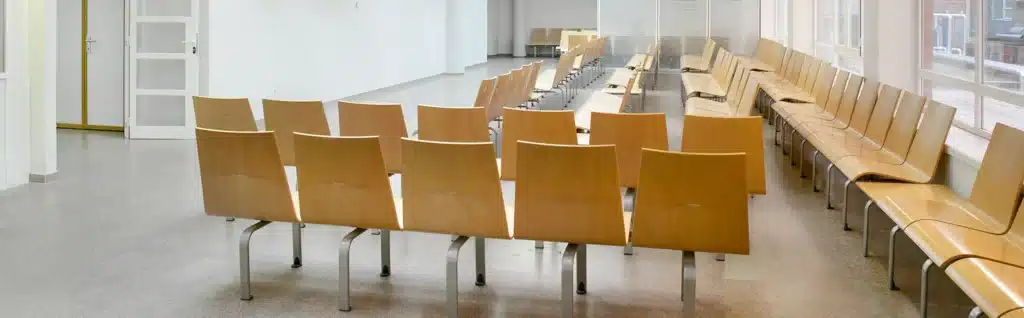 Empty UK GP Clinic waiting room with wooden chairs fixed to the floor