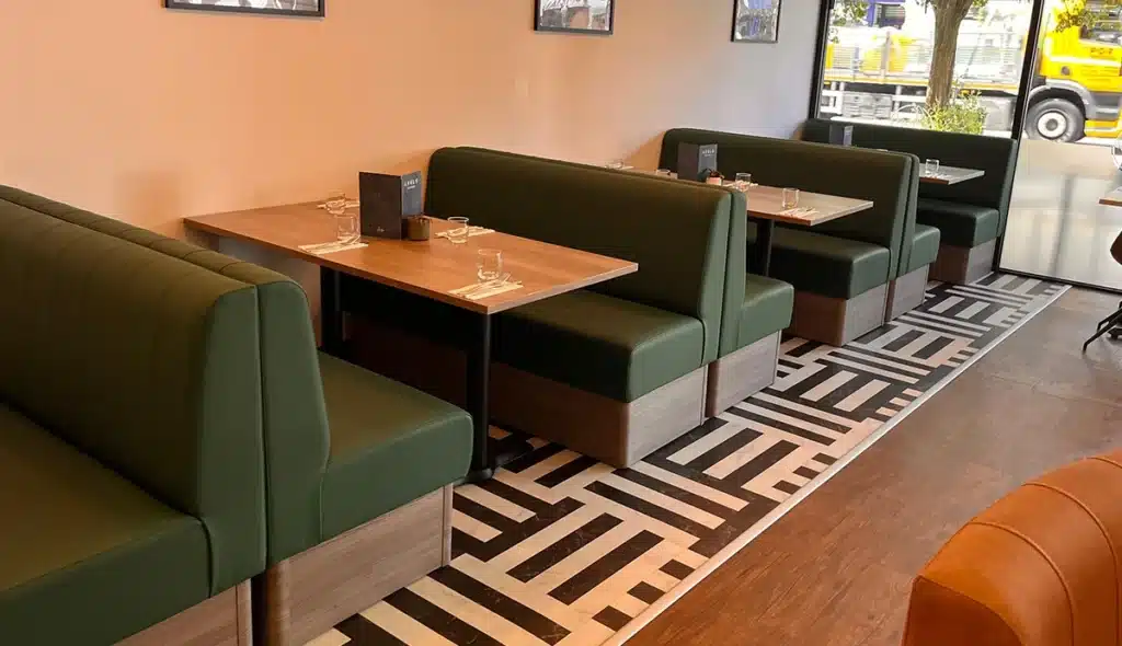 A bright cafe interior with oak dining tables inbetween back to back booth sets