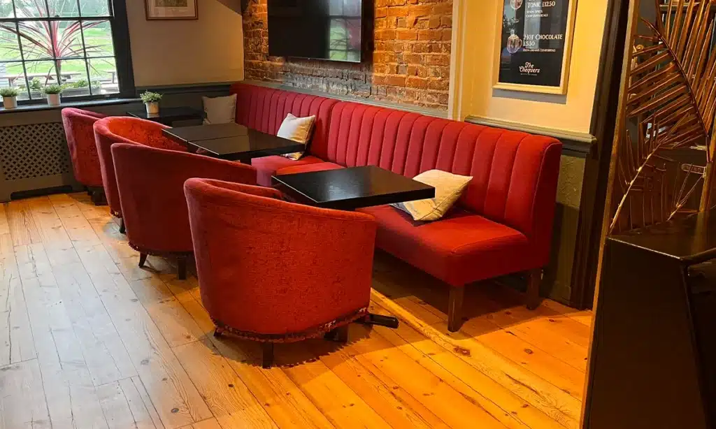 Dark Red deep fluted banquette seating along a wall in a pub, with tables and large tubs opposite