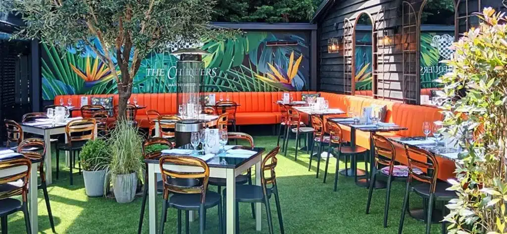 Outdoor pub terrace with tables and chairs, large L shaped banquette seating surrounds the area
