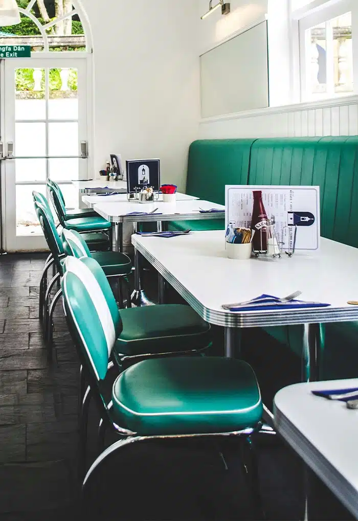 Diners seating area with green vinyl chairs and white tables in a bright retro cafe setting.by HCF Contract Furniture